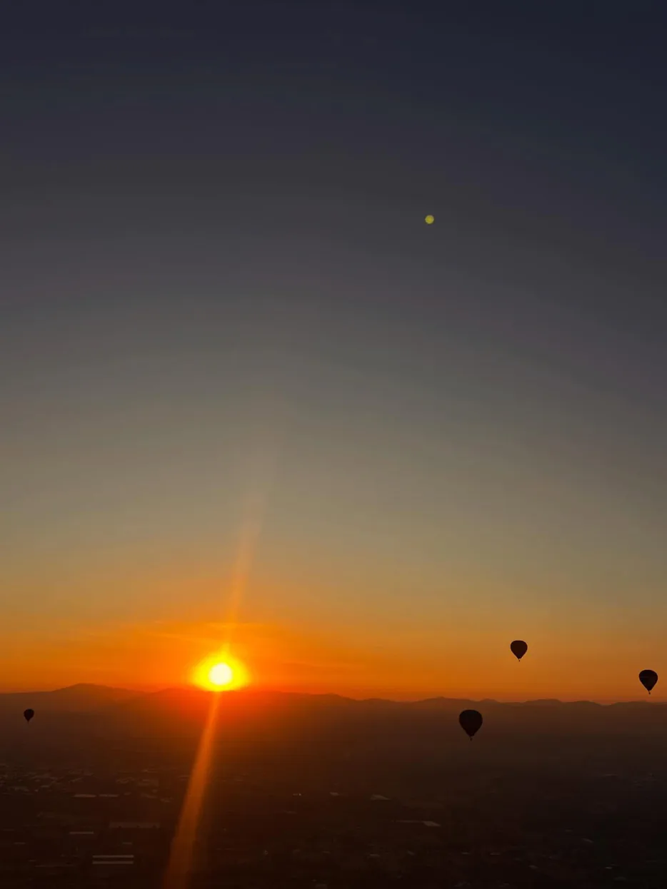 Silueta de un globo aerostático frente al sol naranja del amanecer en Teotihuacán