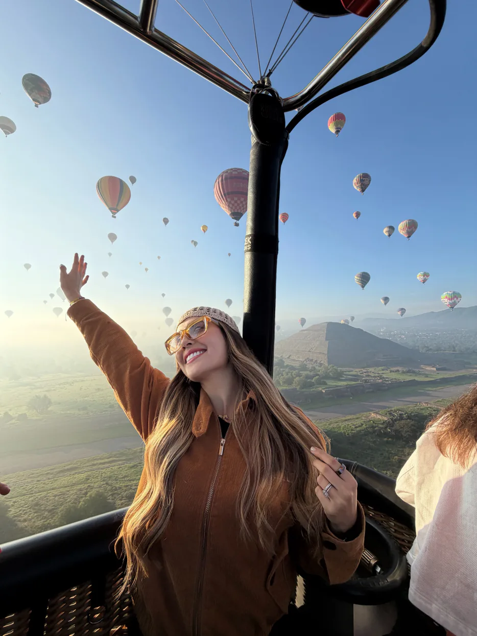 Mujer con los brazos en alto dentro de la canasta del globo durante el amanecer en Teotihuacán